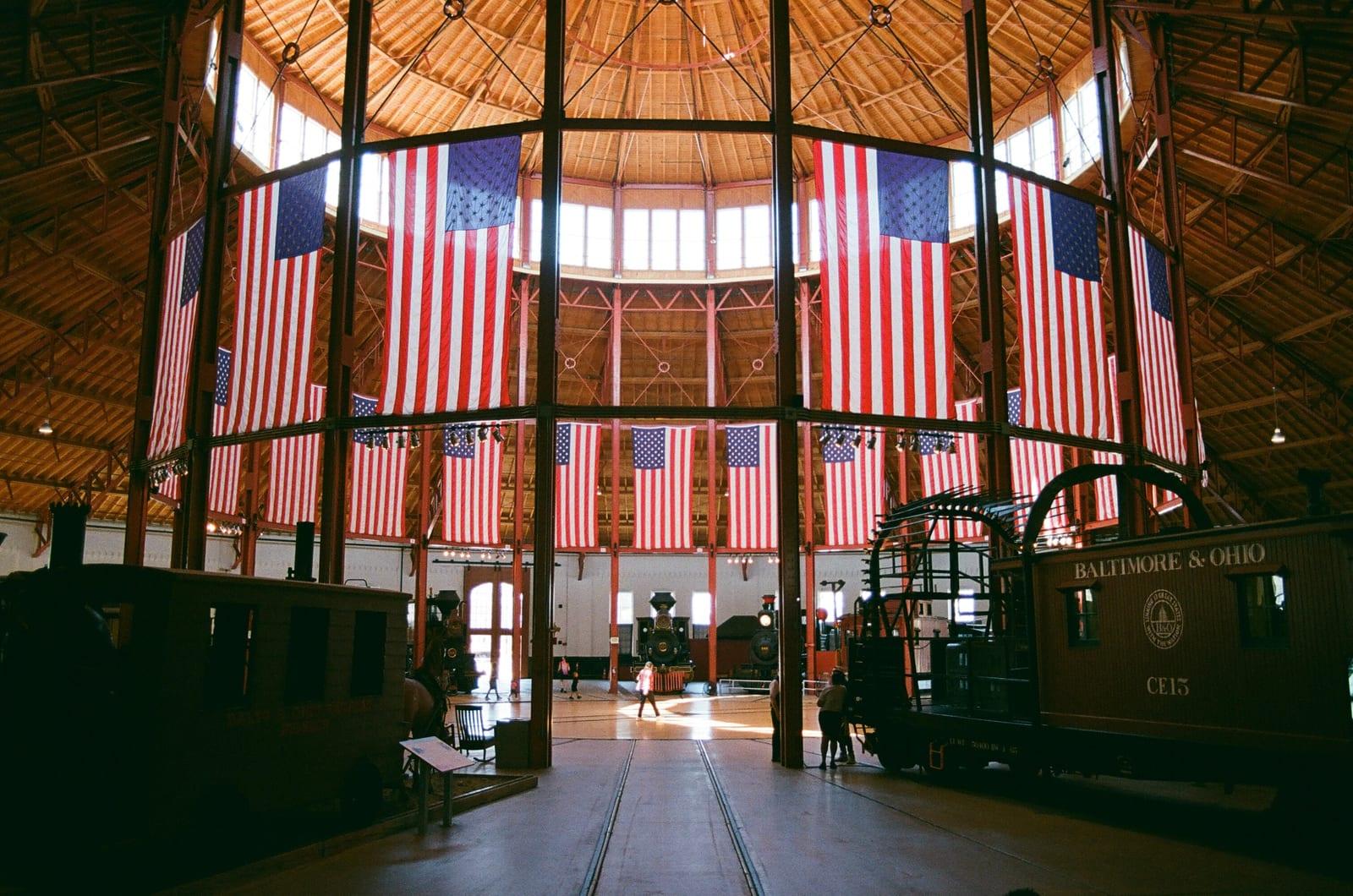 Inside the museum's roundhouse: iron columns under the timber roof, American flags hung between them, and old Baltimore & Ohio cars on the tracks