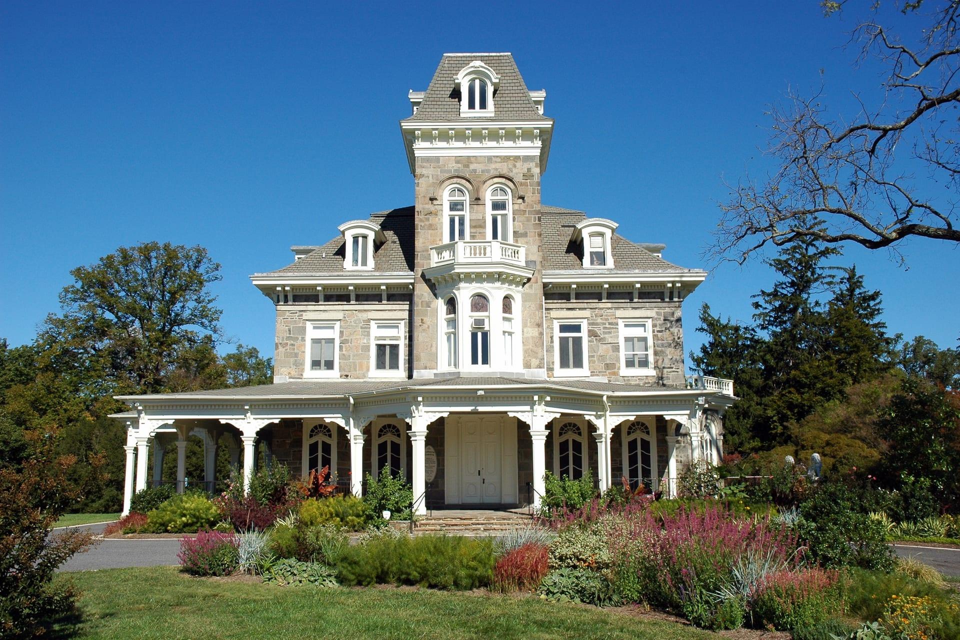 The stone front of Cylburn Mansion behind its planted border, under its long veranda
