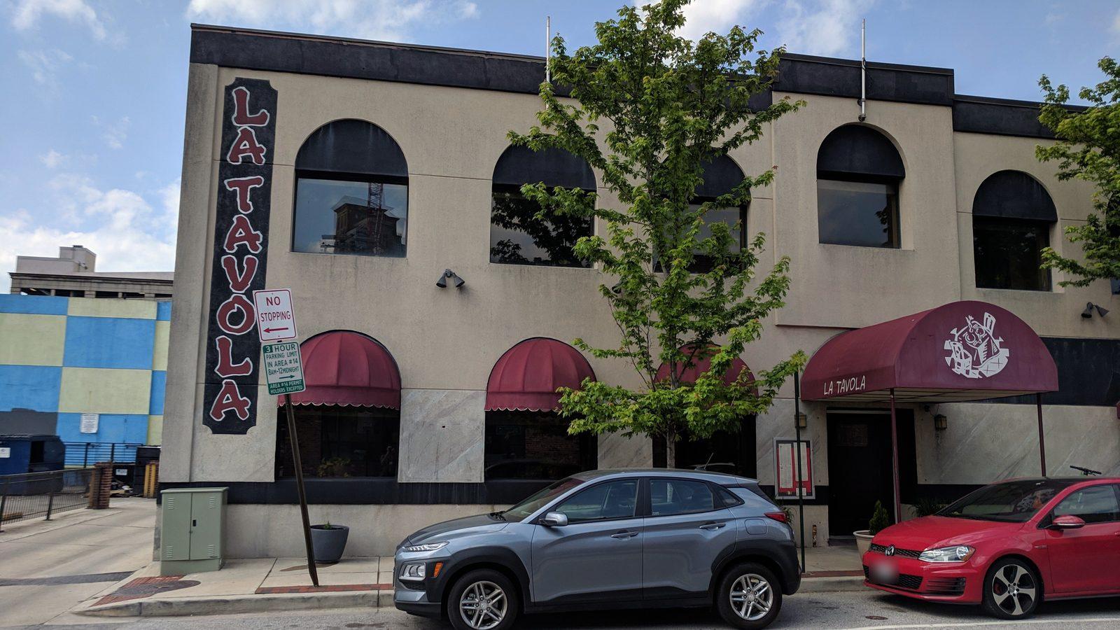 La Tavola's front on Albemarle Street in 2019: the tall black sign, the arched windows and the burgundy awning over the door