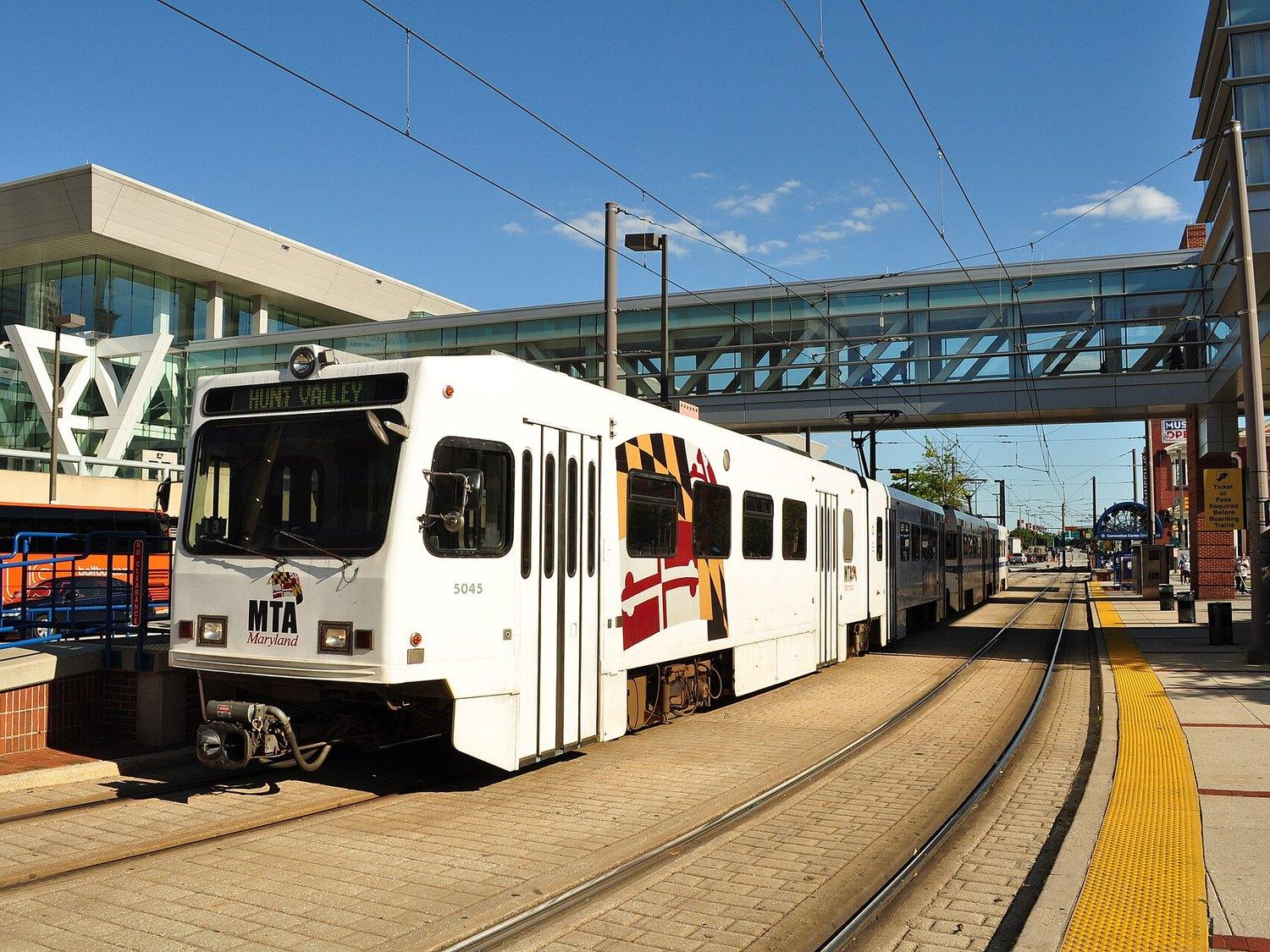 A white and grey MTA light rail car at a street-level platform, the track running away down the middle of the road