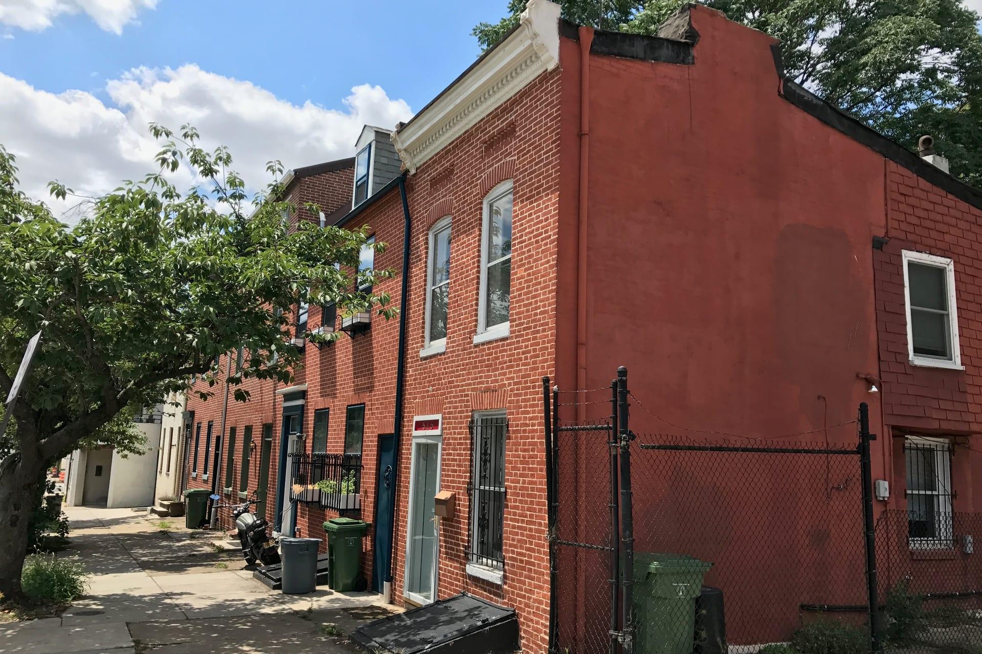 Brick rowhouses on North Paca Street, one end wall painted red, a tree over the pavement