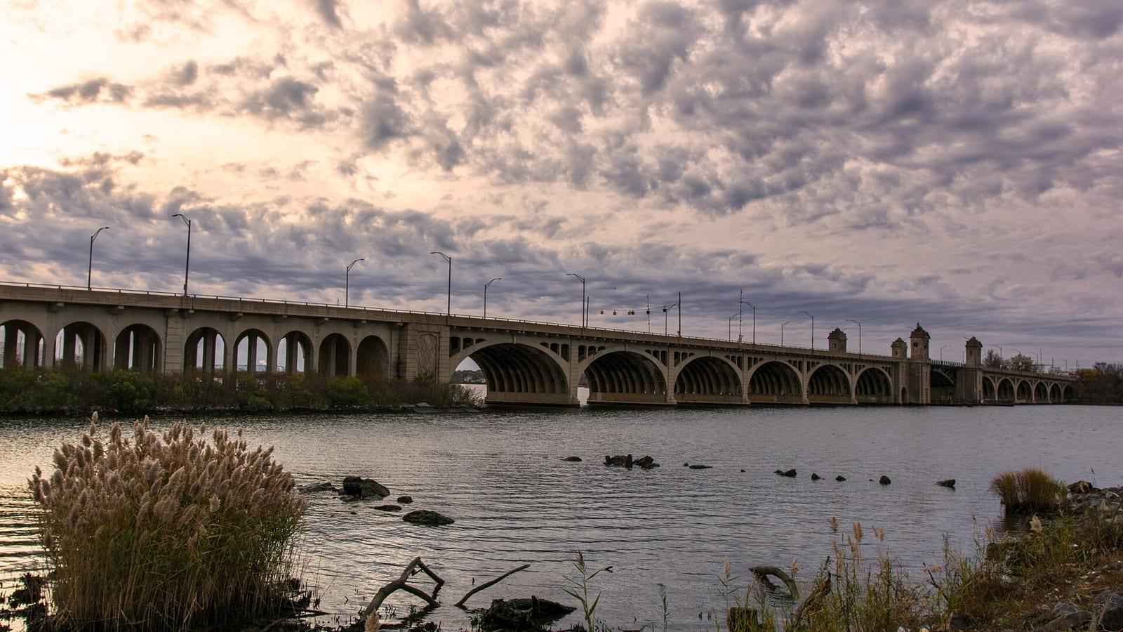 The arches of the Hanover Street Bridge across the Middle Branch at dusk, tall grass on the shore in front