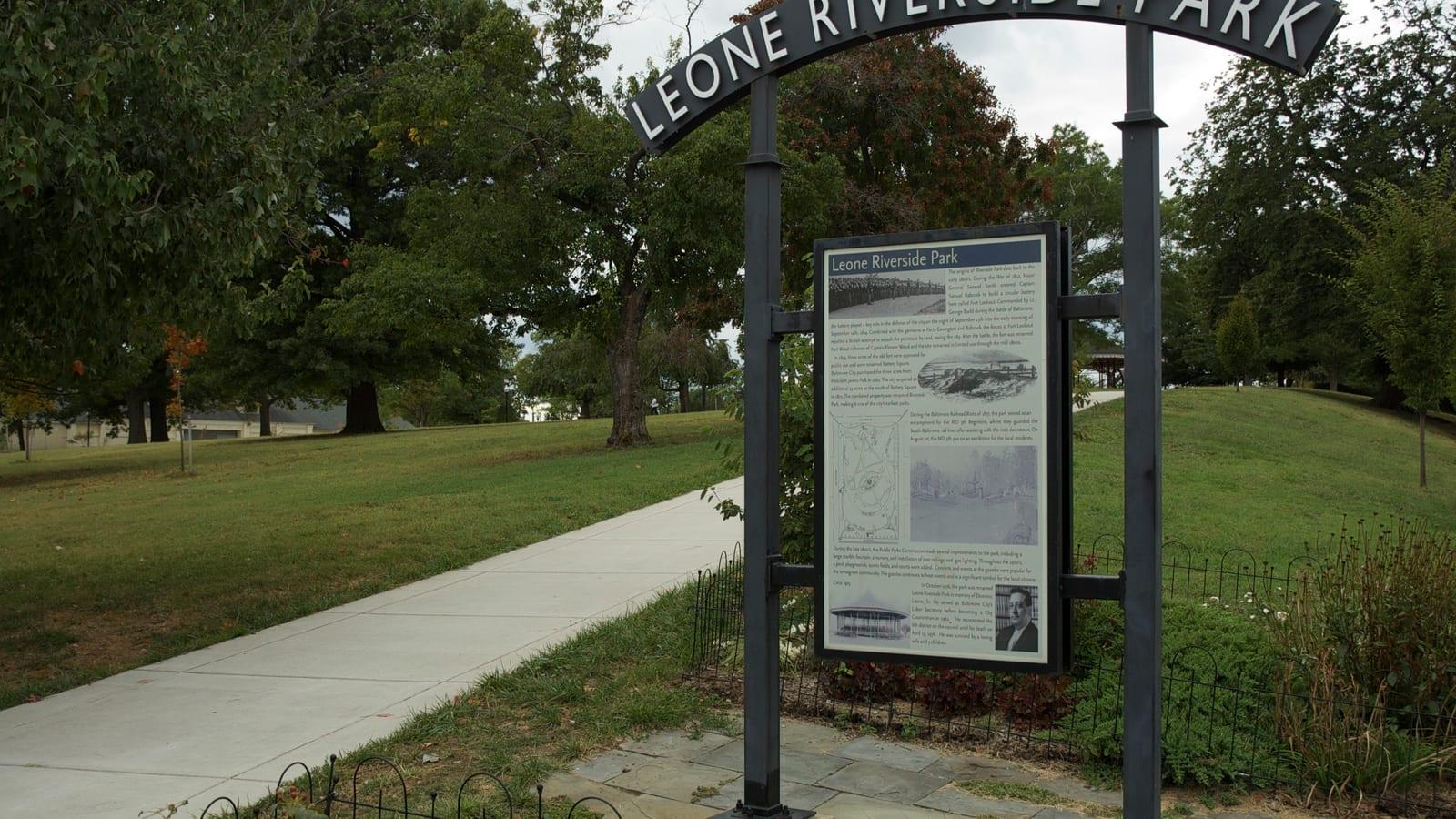 The iron entrance arch of Leone Riverside Park, its name across the top, lawns and old trees behind