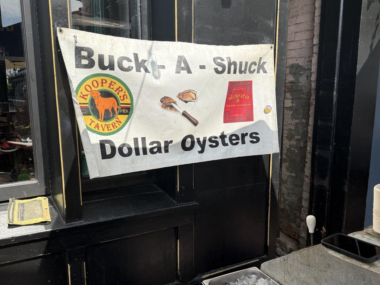 The Buck-A-Shuck dollar oysters banner on Slainte's black and gold front, a tray of oysters on ice below it