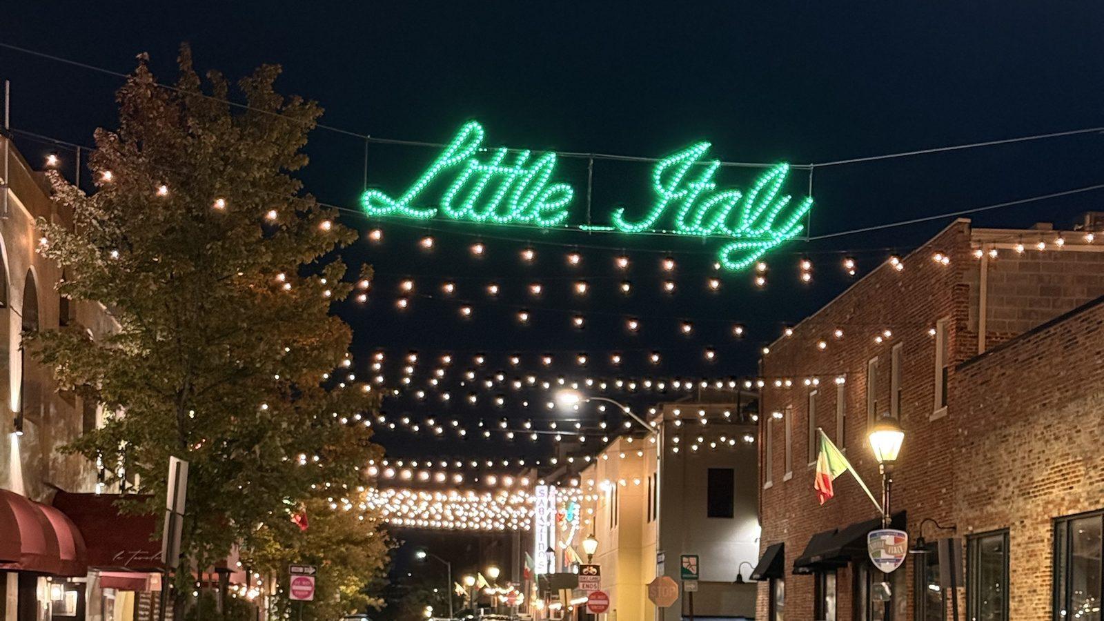 Little Italy's green neon sign and strings of lights across the street at night, La Tavola's awning on the left and Sabatino's sign down the block